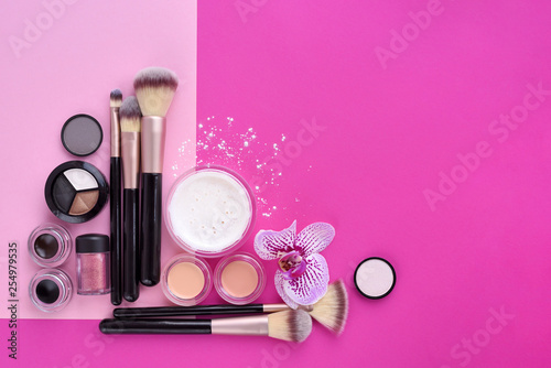 Makeup brush and decorative cosmetics and a orchid flower on pink background. Top view