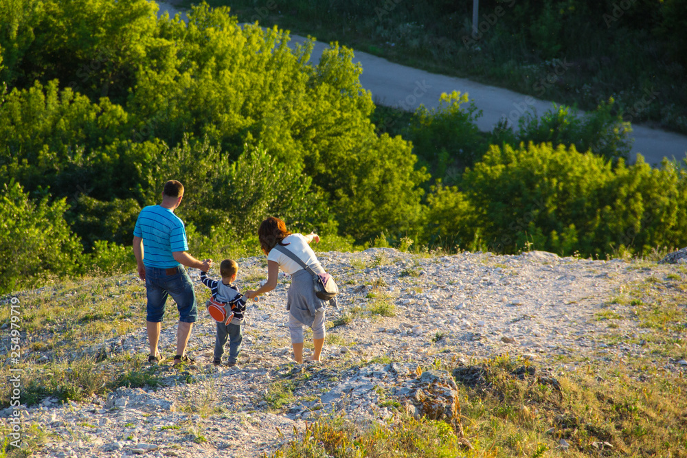 A young family consisting of mom, dad and child are walking down the stones from the mountain against the background of the forest, holding hands.