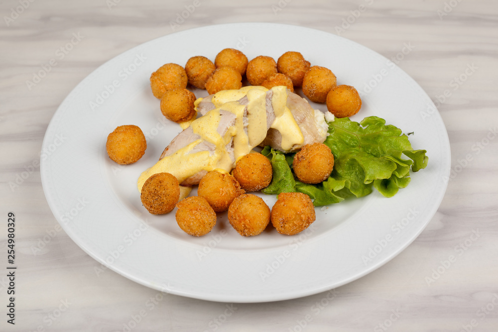 Fried potato balls and chicken fillet with green salad on a white plate. Fried potato balls and chicken fillet with green salad on a white plate.