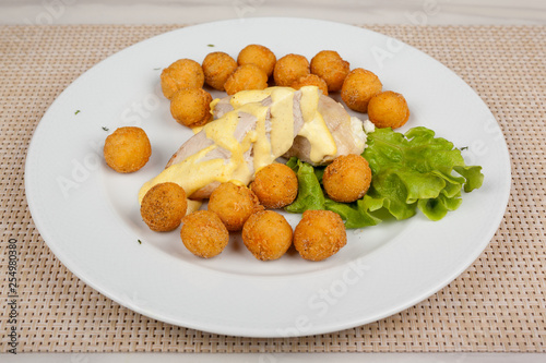 Fried potato balls and chicken fillet with green salad on a white plate.