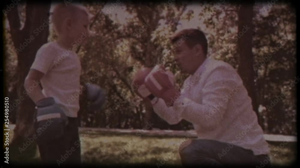 Family video archive. Retro camera 8 mm. Old film. Father and son in boxing gloves play boxing on the lawn near the house. happy childhood.