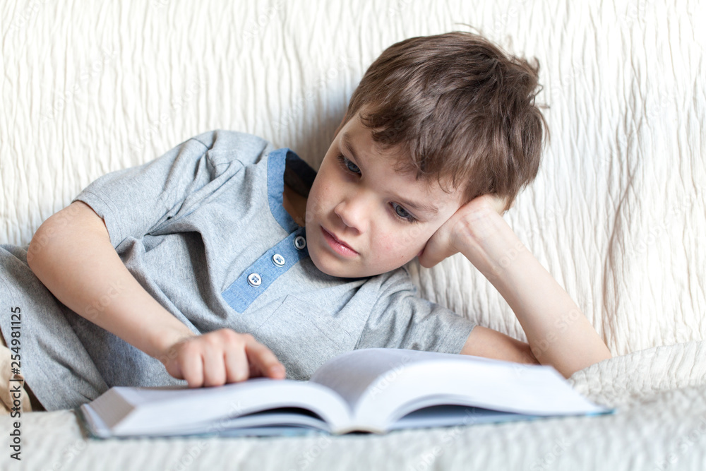 Boy reading a book on the couch in the room Boy reading a book on the couch in the room