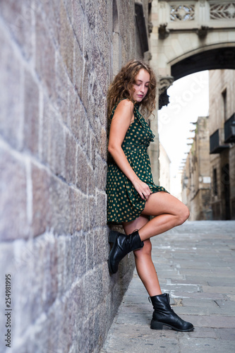 Young sexy woman in dress standing near the stone wall and showing legs