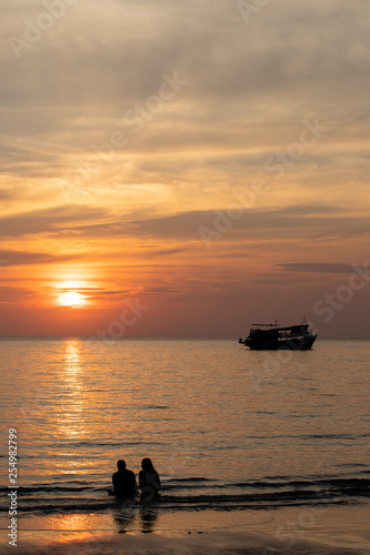 Verliebtes Paar am Strand mit Blick auf Sonnenuntergang und Fischerboot