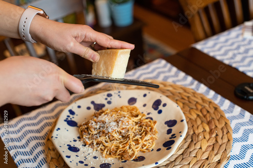 woman hands grating parmesan cheese to homemade spaghetti bolognese, traditional pasta dish with meat and vegetables