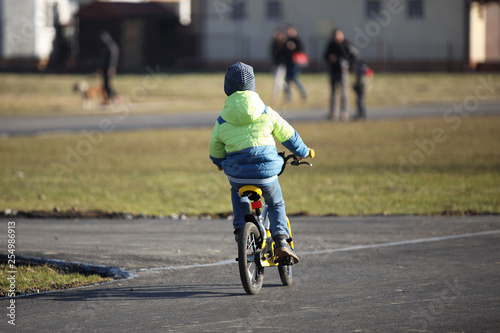 A boy in demi-season clothing rides a bicycle on an asphalt road. The younger generation is engaged in sports and actively spends free time in the fresh air. Games on the street. Children s joy