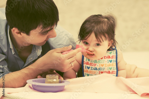 Happy young father feeding baby girl on blanket at home