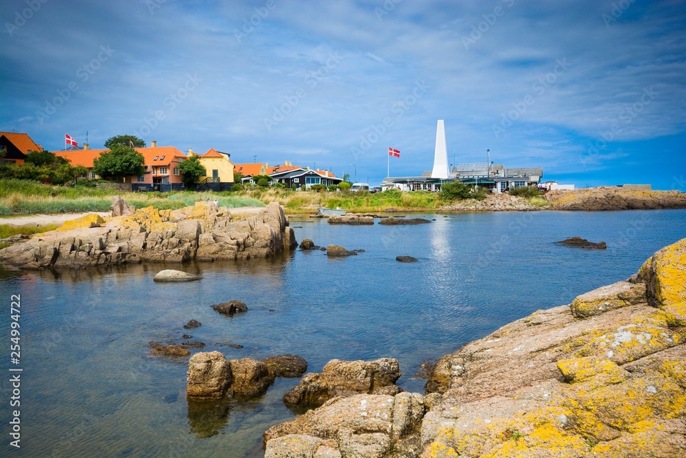 Rocky coast of Baltic Sea in Allinge, Bornholm, Denmark. Chimney of smokehouse in the background