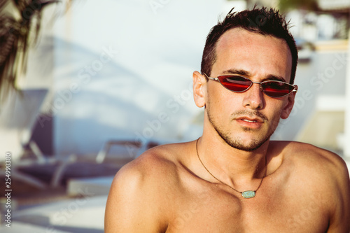 Portrait of a handsome young man in glasses chilling in the swimming pool. Perfect hair & skin. Outdoor shot.