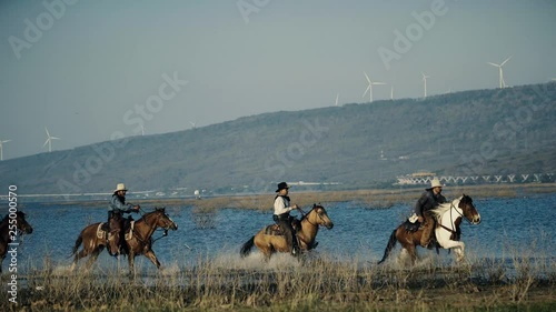 Cowboys riding horses in wild field and river at evening