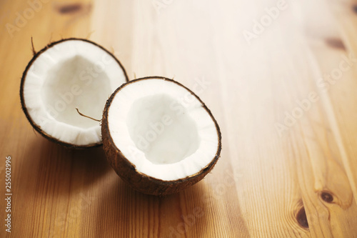 Halved coconut on wooden table in white light. Hello summer vacation concept. Space for text. Tropical background with coconut. Delicious nut, refreshing drink and oil source, tasty milk