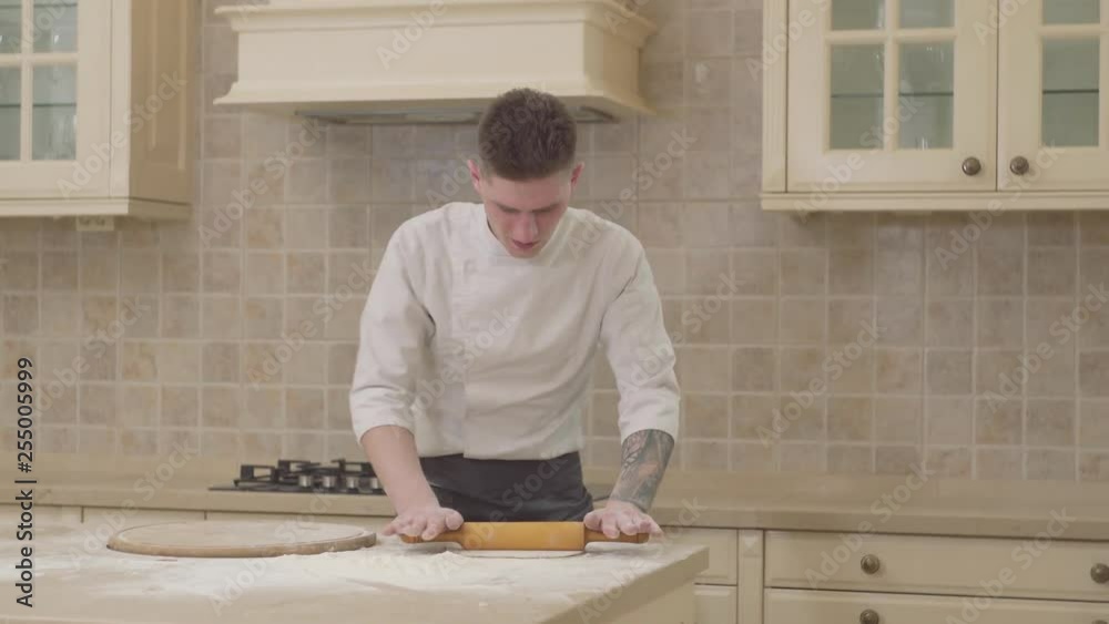 Rolling dough with rolling pin for pizza preparation on table. Chef rolling dough for pie with wooden roller. Baking bread and cake in bakery. Chef cook cooking food on kitchen table Rolling dough with rolling pin for pizza preparation on table. Chef rolling dough for pie with wooden roller. Baking bread and cake in bakery. Chef cook cooking food on kitchen table