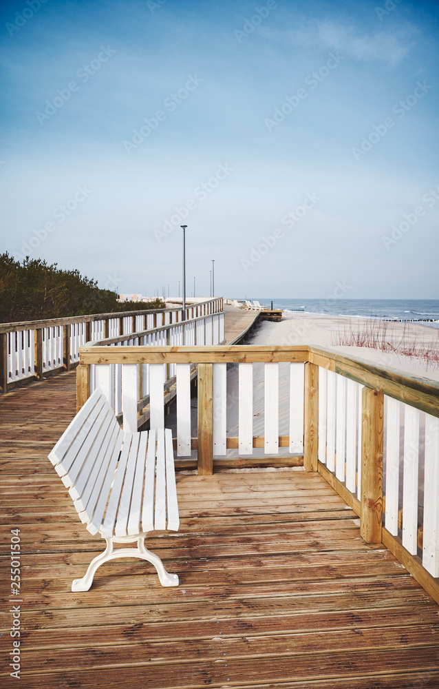 Naklejka premium Empty bench on a wooden boardwalk by a beach
