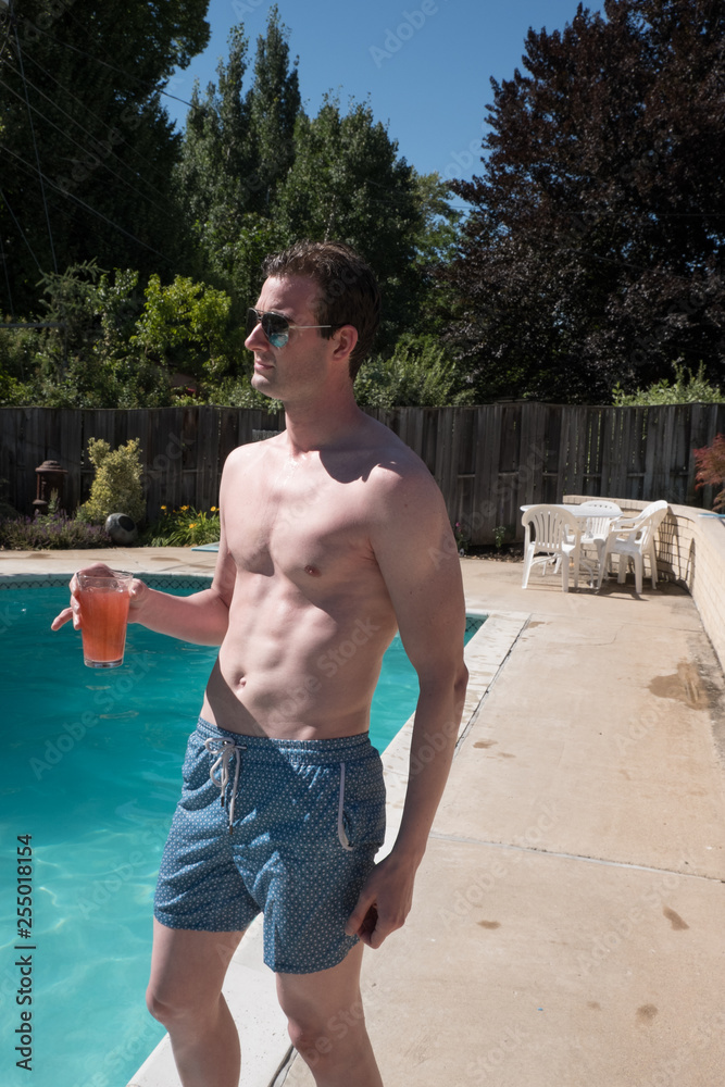 Fit Caucasian man with defined abs standing on deck of an outdoor swimming  pool in blue