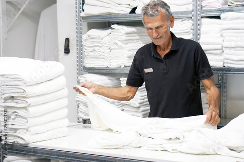 Fotografie Elderly caucasian male laundry hotel worker folds a clean white towel