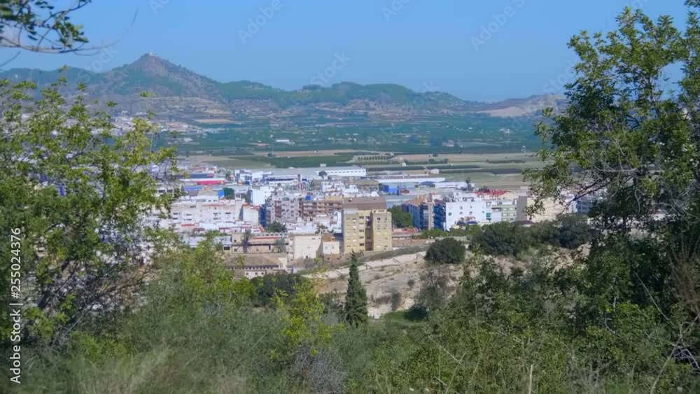 Small provincial town at the foot of the mountains in Spain. The orange color tile of roofs the houses are clearly visible from the mountain. The walls of the ancient castle descend from the mountains