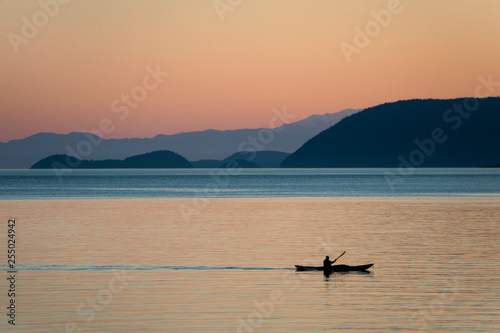 Kayaking at Sunset Through the San Juan Islands of Washington State. A kayaker paddles past Orcas Island in the Salish Sea during a beautiful sunset.