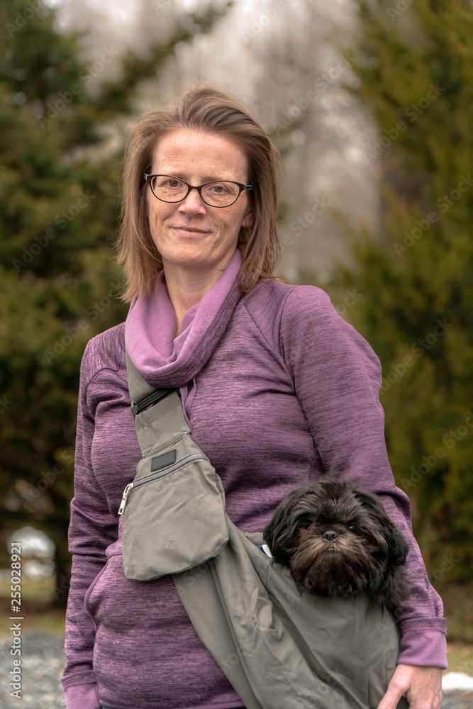 Beautiful woman carrying black shih tzu puppy dog in shoulder bag