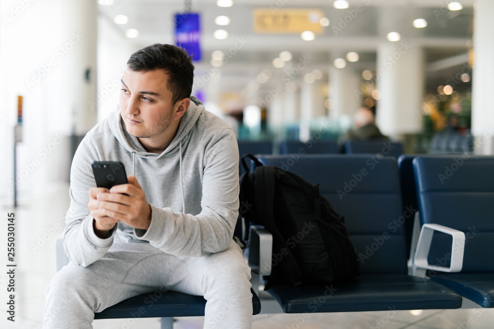 Texting he is fine. Portrait of handsome smiling man in casual wear holding his luggage and messaging through his mobile phone while sitting in the hall of the airport Texting he is fine. Portrait of handsome smiling man in casual wear holding his luggage and messaging through his mobile phone while sitting in the hall of the airport