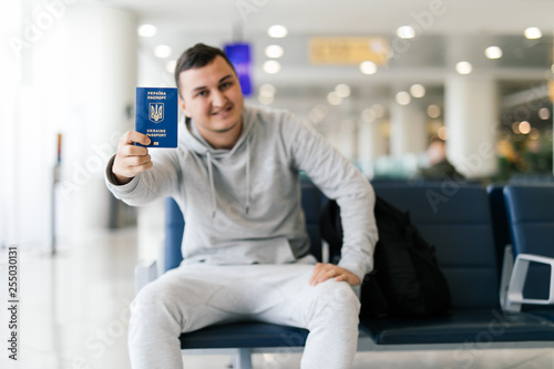 Young Man waiting at an airport, holding ukrainian passport in an airport