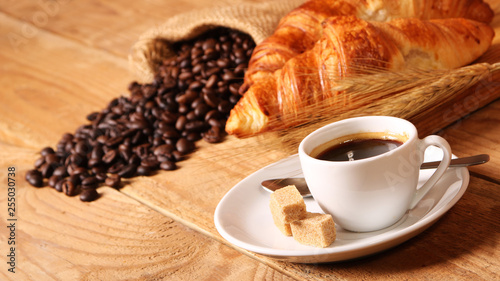 Coffee white cup, croissants on wooden table and roasted coffee beans. Breakfast concept