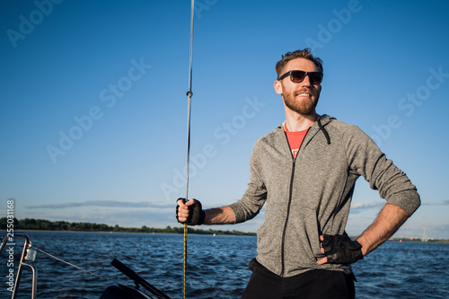 Young european man standing at edge of yacht looking at sea. Travelling on old boat with sail. Luxury lifestyle.
