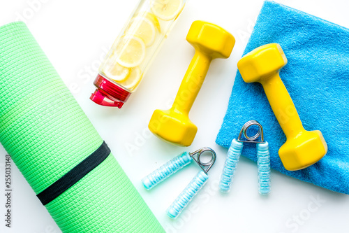 workout with bars, mat, bottle of water and wrist builder yellow background top view