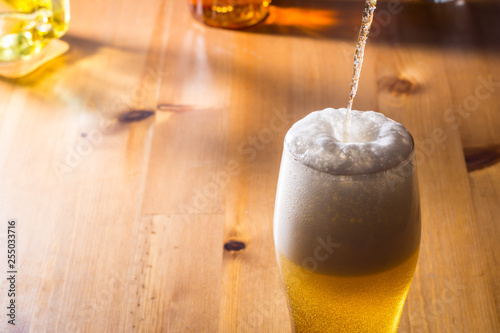 Beer is poured into a glass on a wooden table. photo