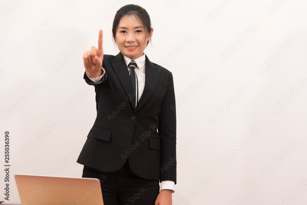 Beautiful office woman stand at table in office ,she show forefinger for successful work,search information on notebook,look friend and smile agreement.business concept. Beautiful office woman stand at table in office ,she show forefinger for successful work,search information on notebook,look friend and smile agreement.business concept.