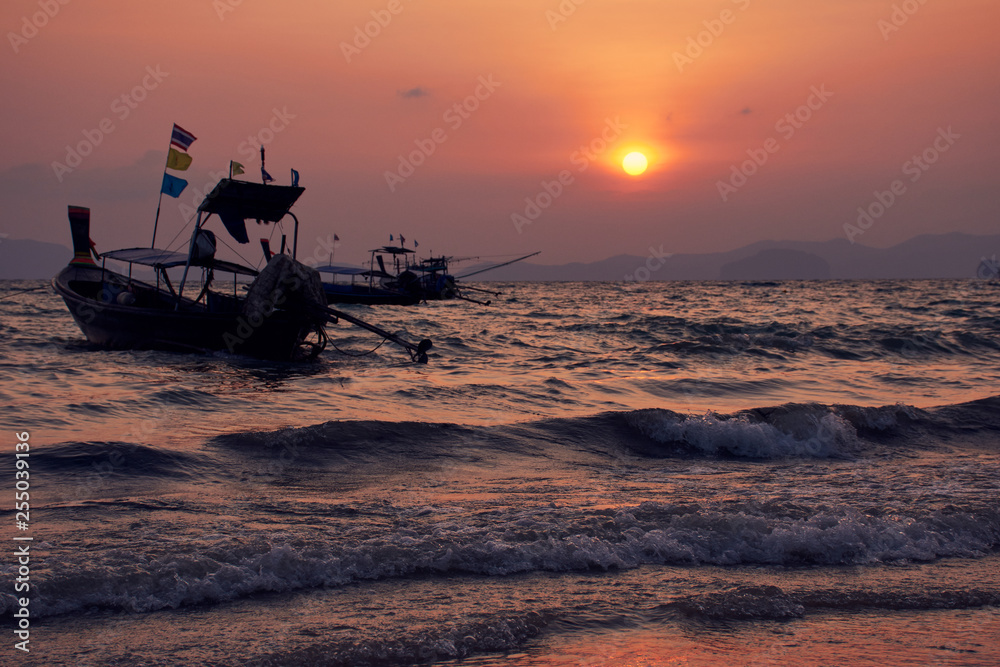 Long-tailed boat in wavy sea during sunset at Khlong Muang Beach, Krabi, Thailand.