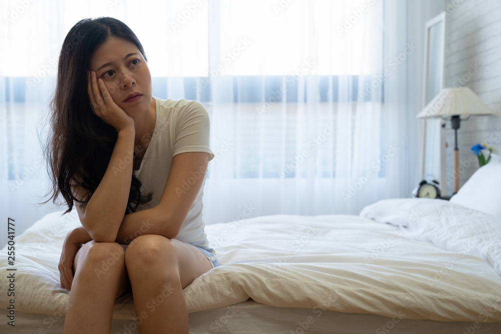 Stressed sad beautiful woman sitting on bed in cozy bedroom at home. Disappointment depression anxiety and disorder concept. worried young girl in comfort shirt thinking thoughtful problems indoors. Stressed sad beautiful woman sitting on bed in cozy bedroom at home. Disappointment depression anxiety and disorder concept. worried young girl in comfort shirt thinking thoughtful problems indoors.