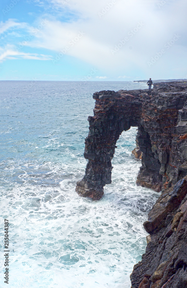 Tourist walking on Holei Sea Arch, Big Island, Hawaii Volcanoes National Park.  Lava rock Arch Formation