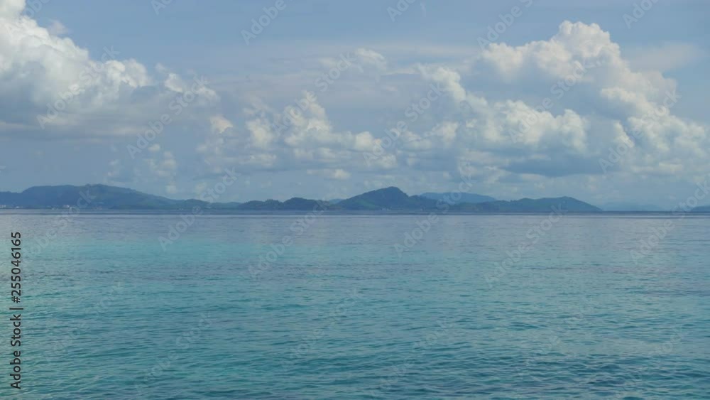locked shot of beautiful wide calm turquoise ocean with mountain shore line on horizon, daylight, blue white cloudy sky with cumulus formations locked shot of beautiful wide calm turquoise ocean with mountain shore line on horizon, daylight, blue white cloudy sky with cumulus formations