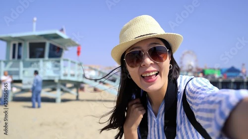 fast motion chinese girl blogger recording travel trip video in usa hand gesture showing safeguard stand on beach bay Santa Monica Pier. tourist with sunglasses talking on video phone call mobile