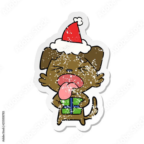 distressed sticker cartoon of a dog with christmas present wearing santa hat