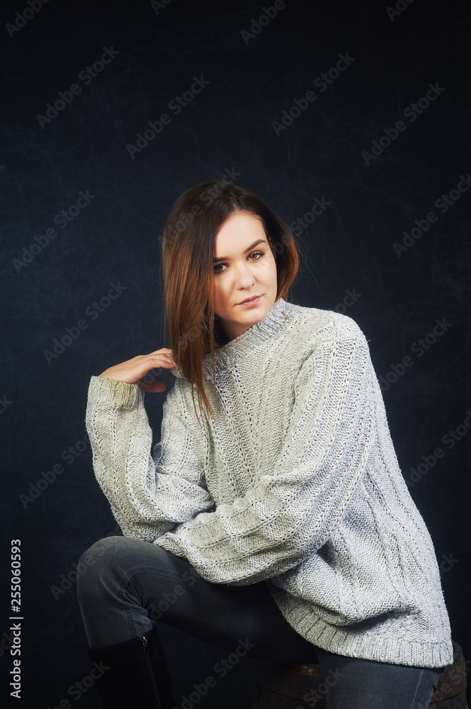 Studio portrait of a young woman on a dark background . The girl is dressed in a warm knitted sweater Studio portrait of a young woman on a dark background . The girl is dressed in a warm knitted sweater