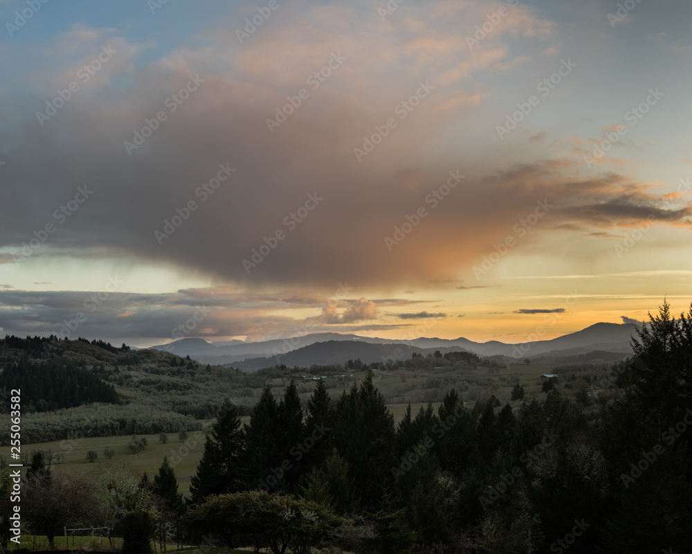 Sunset over Oregon's Willamette Valley with Oak trees on Bald Hill, and farmland, and Douglas Fir trees in the foreground.