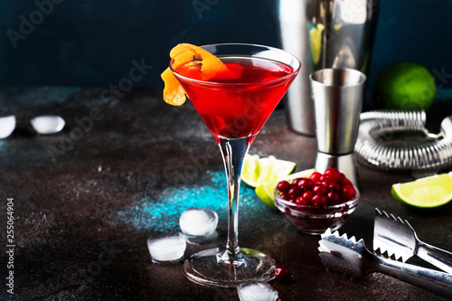 Classic alcoholic cocktail cosmopolitan with vodka, liqueur, cranberry juice, lime, ice and orange zest, dark bar counter background, night mood, space for text