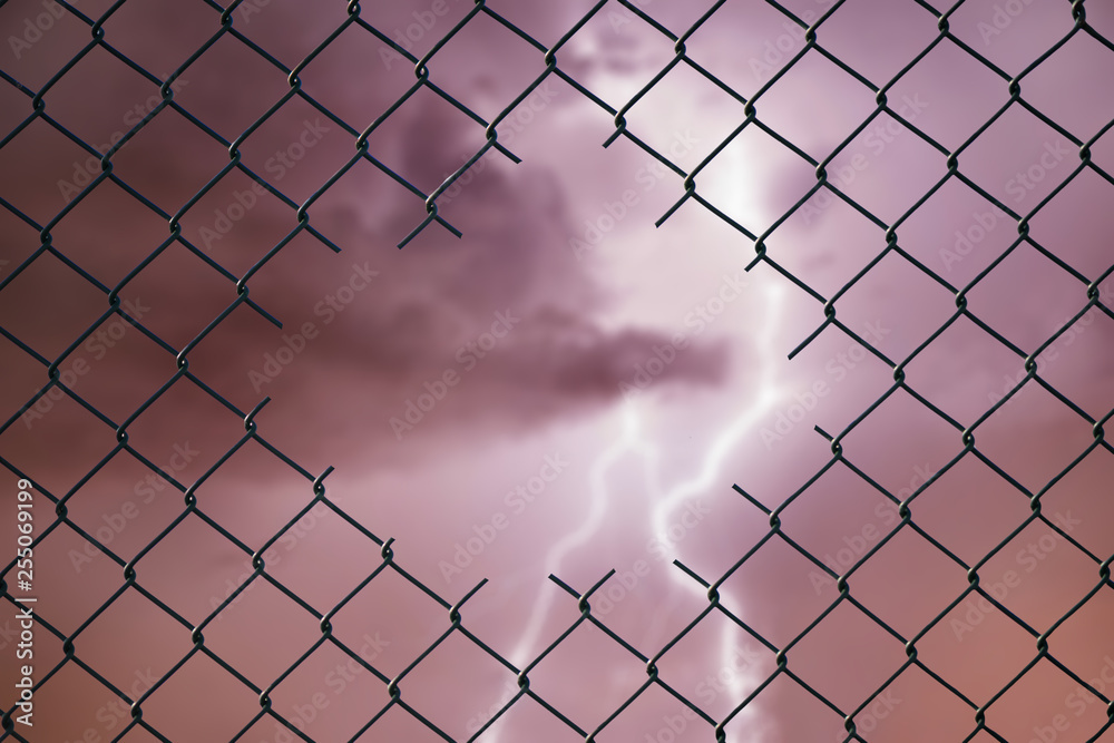 Conceptual image of lightning in the stormy sky and steel mesh wire fence. Concept of hope and freedom Conceptual image of lightning in the stormy sky and steel mesh wire fence. Concept of hope and freedom