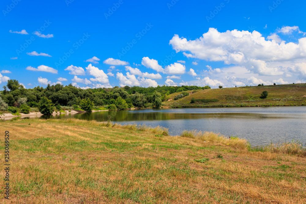 Summer landscape with beautiful lake, green meadows, hills, trees and blue sky