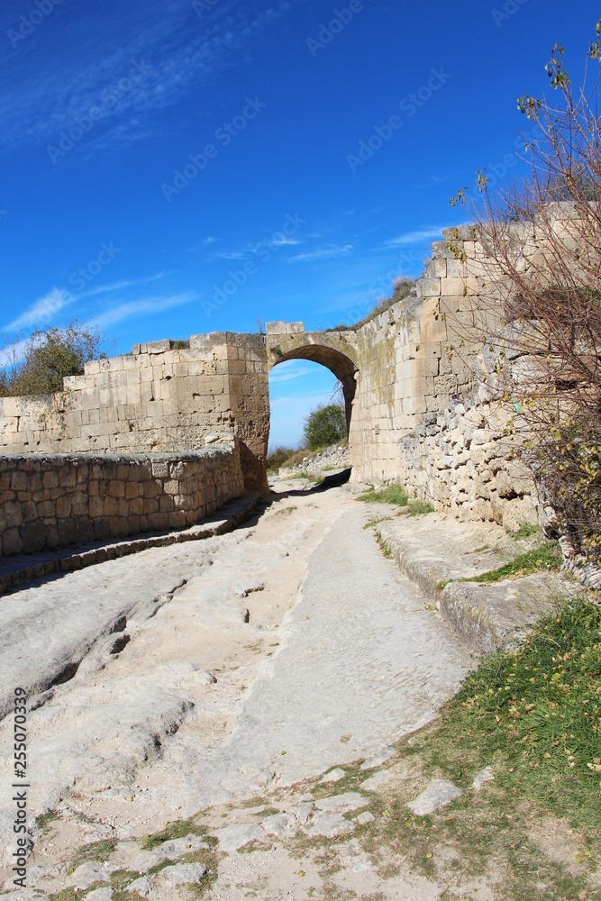 Obraz premium The central street of the cavecity Chufut-Kale. Above the road is visible arch, left from the gate in the fortified wall. It's a medieval city-fortress in the Crimean Mountains that now lies in ruins.