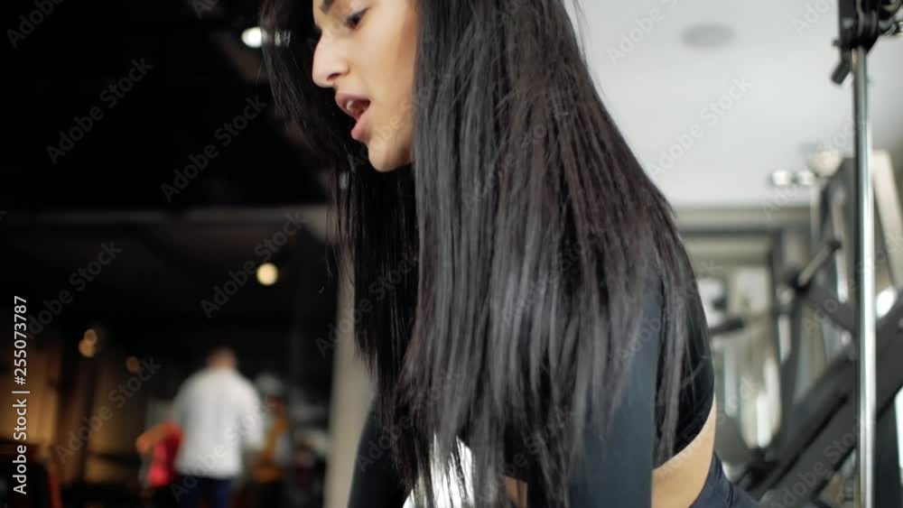 Attractive young caucasian girl doing biceps exercises while sitting on the bench and raising dumbbell in the gym Attractive young caucasian girl doing biceps exercises while sitting on the bench and raising dumbbell in the gym