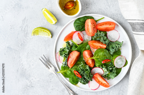 fresh salad of organic spinach, kale, tomatoes and radish with olive oil and lime juice. healthy eating concept. diet, vegan cuisine. light background, selective focus