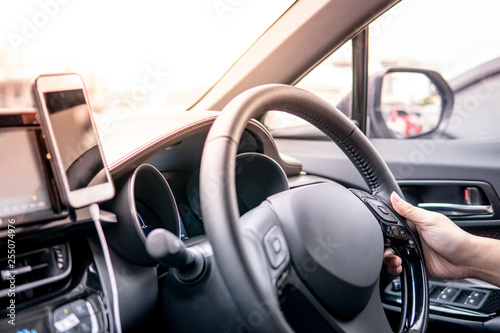 Male driver hand holding on steering wheel using smartphone for GPS navigation. Mobile phone mounting with magnet on the car console in modern car. Urban driving lifestyle with mobile app technology © zephyr_p