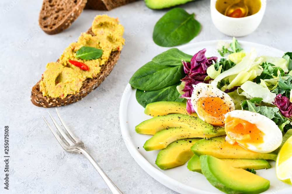 food for a healthy Breakfast or lunch. salad of avocado, kale leaves, egg and spinach, on a white plate, grain bread, diet food, organic vegetables, food flat lay