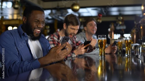 Men in bar celebrating successful bet on sports, using online bookmaker on phone photo