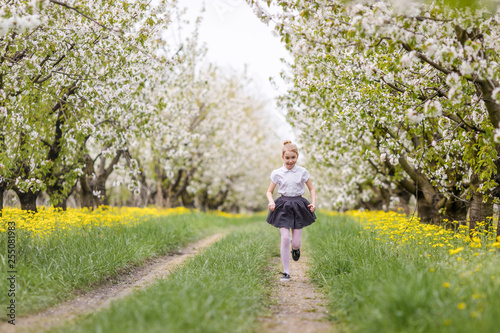 Blonde girl in gray skirt and white shirt playing and running in the cherry blossom garden
