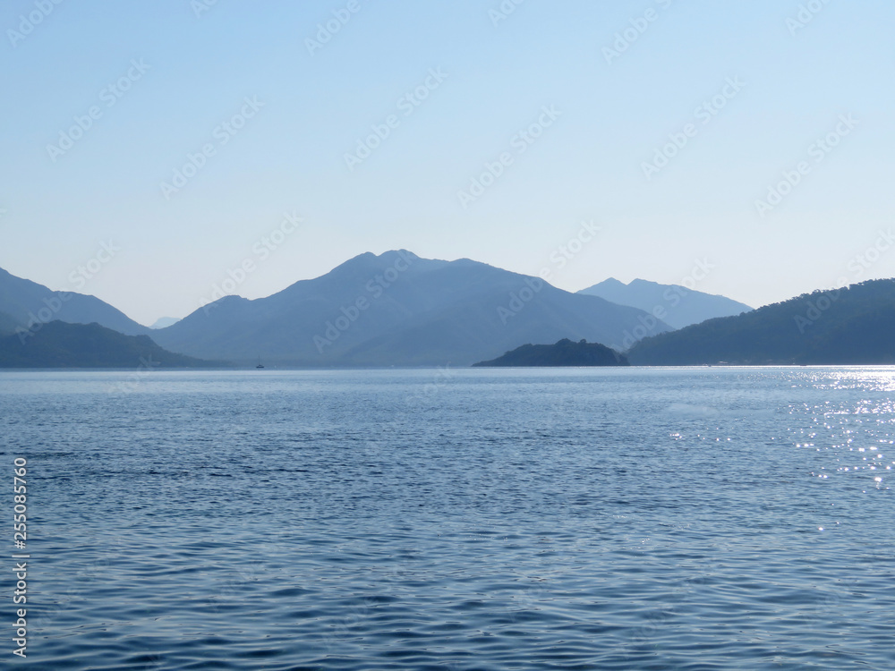 Sea coast in the morning, view from the ocean to the mountainous islands. Picturesque seascape, coastline with mountains and hills covered by forest, beautiful panorama