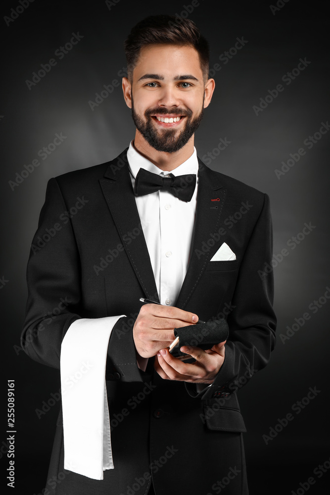 Handsome waiter with notebook on dark background Handsome waiter with notebook on dark background
