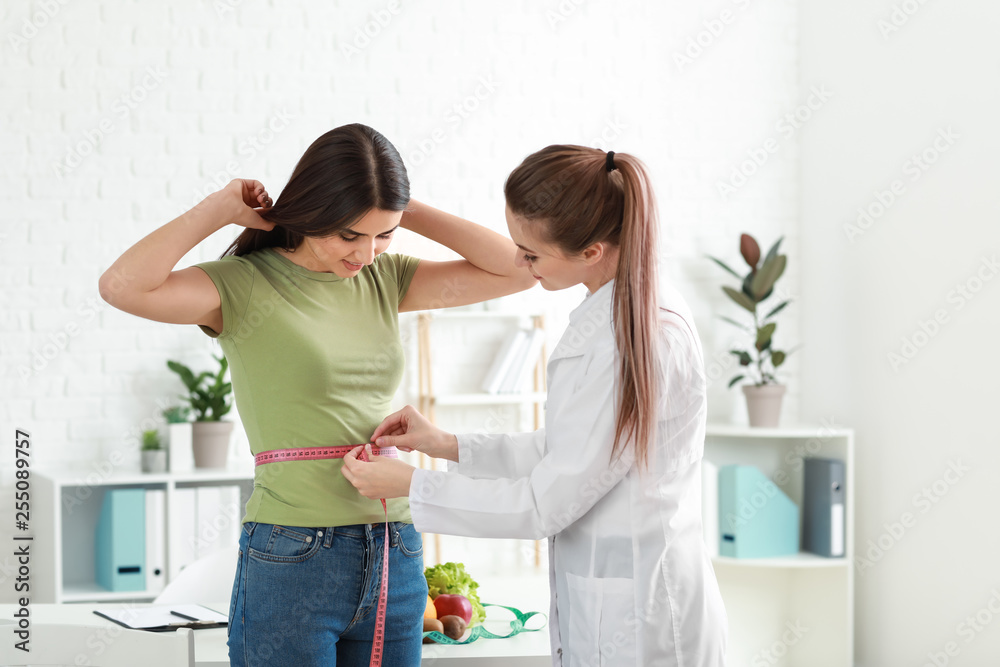 Nutritionist measuring waist of young woman in weight loss clinic - obrazy, fototapety, plakaty 